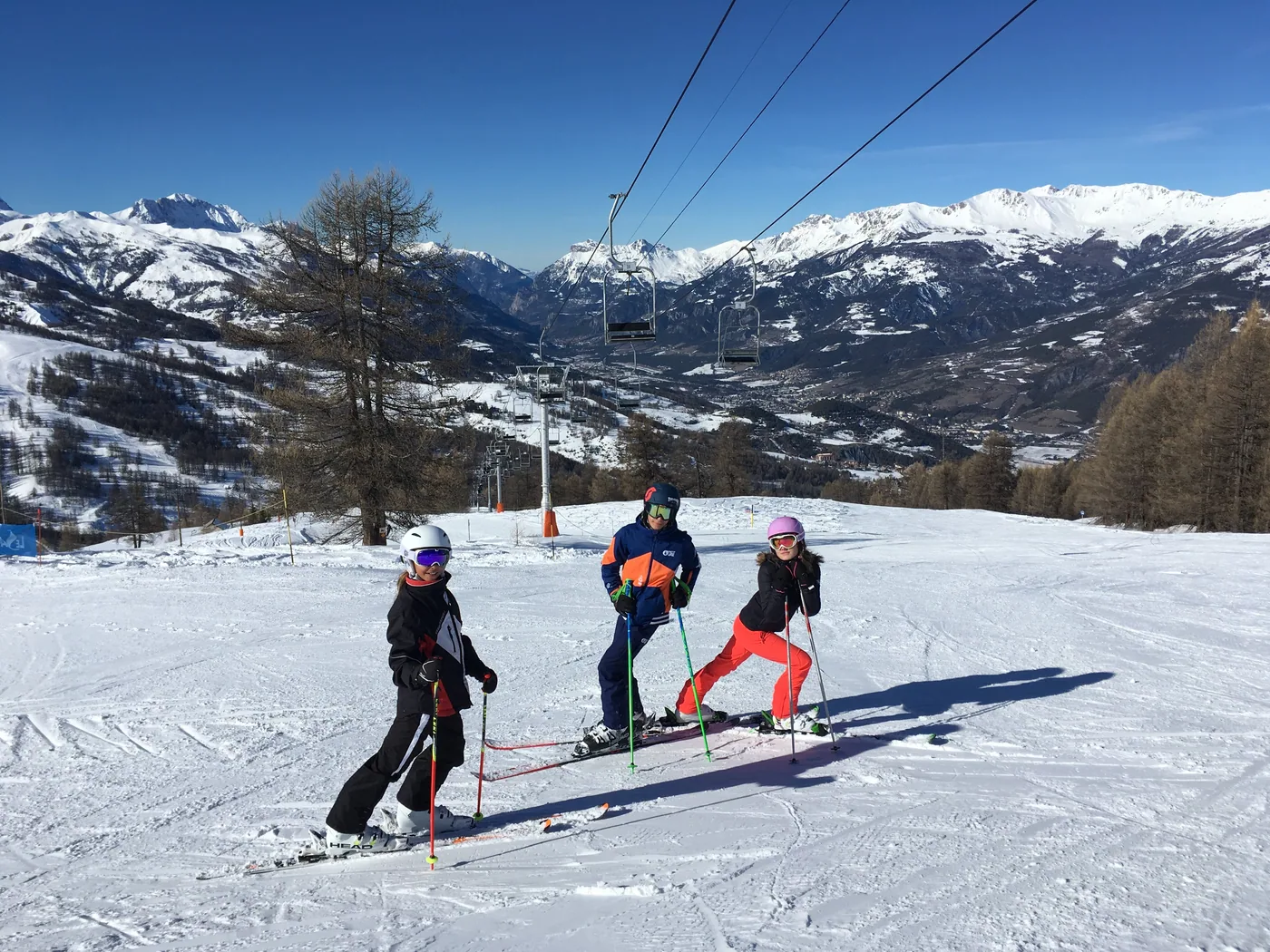 Trois personnes en tenue de ski sur une piste avec panorama alpin
